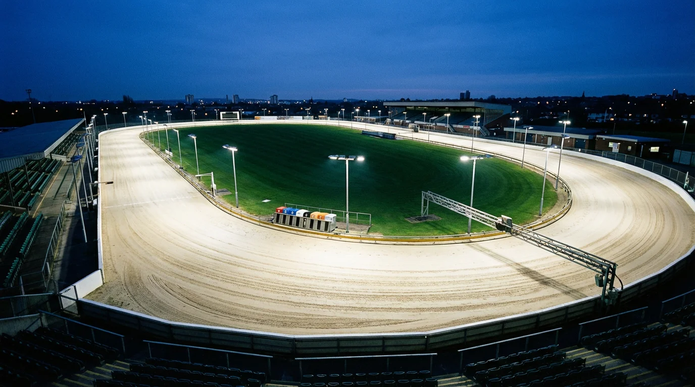 UK greyhound racing track with floodlit sand oval and starting traps at evening meeting